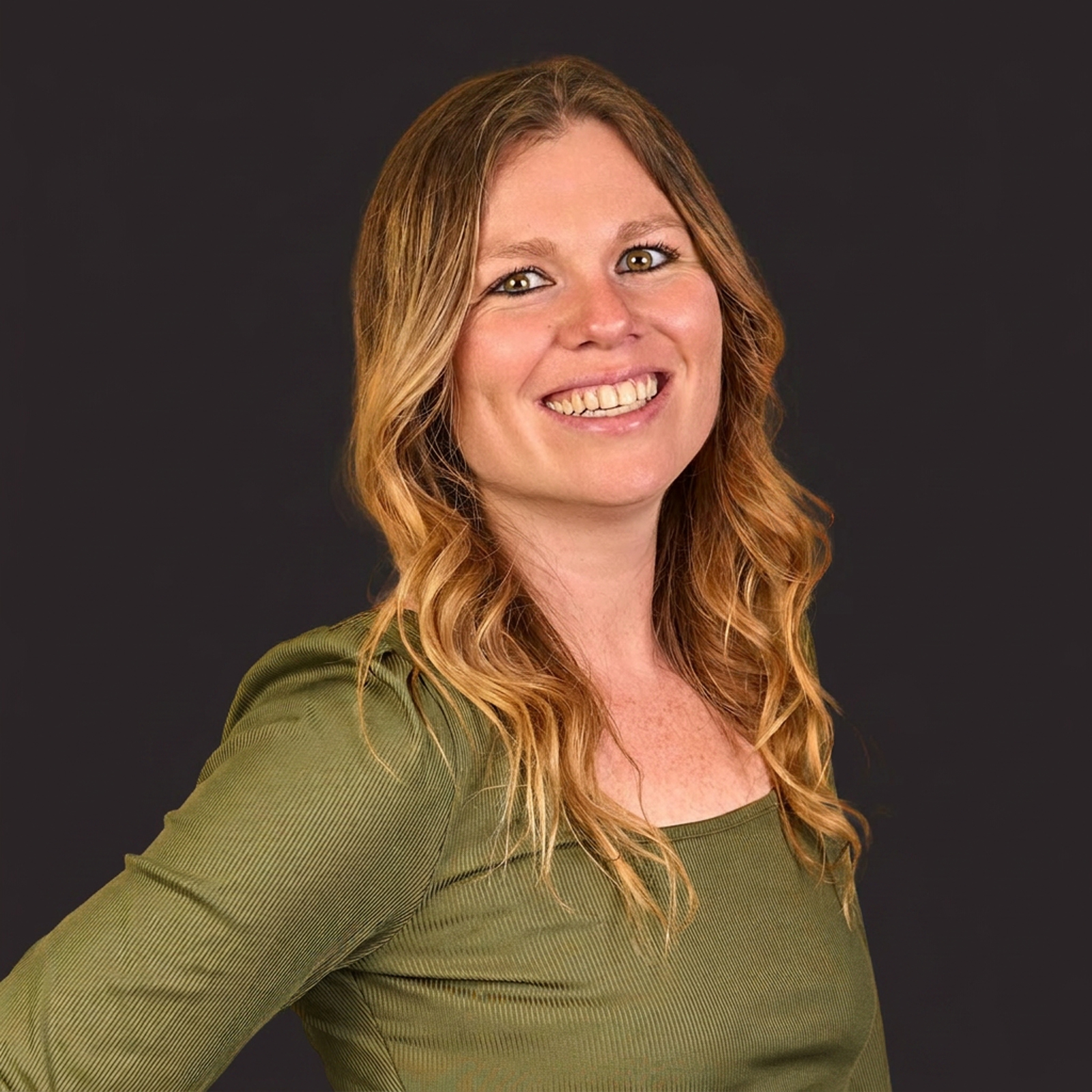 A smiling woman with long wavy blonde hair wearing a green long-sleeve top stands in front of an orange background.